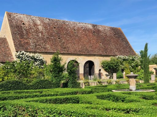 Un jardin historique avec des haies taillées et une vieille bâtisse en pierre.