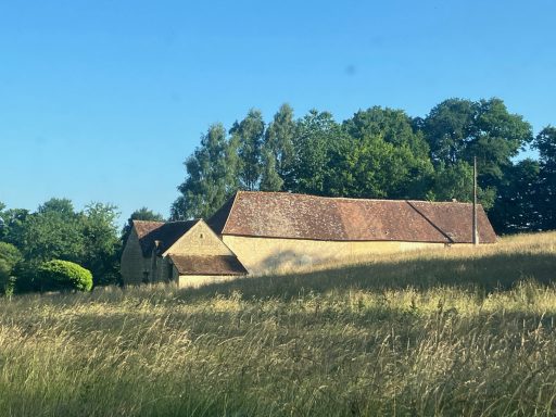 Bâtiment en pierre avec un toit en tuiles, entouré de champs et d'arbres.