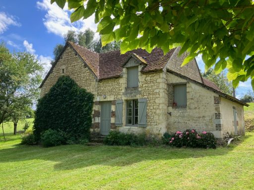 Maison en pierre avec des fenêtres grises, entourée d'arbres et de verdure.