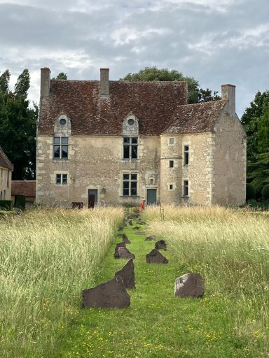 Maison en pierre avec un jardin envahi et des pierres sur le chemin d'accès.