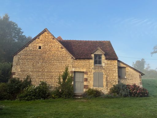 Maison en pierre au milieu d'un brouillard matinal avec des fleurs colorées autour.