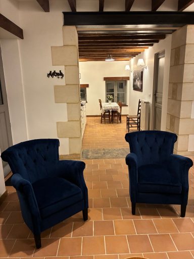 Deux fauteuils bleu en velours placés dans un couloir menant à une salle à manger.