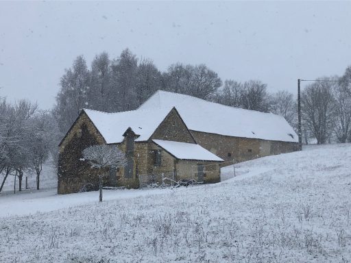 Ferme en bois recouverte de neige, entourée d'un paysage hivernal paisible.