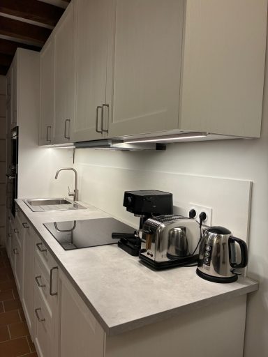 Cuisine moderne avec plans de travail clairs, évier, machine à café et bouilloires.