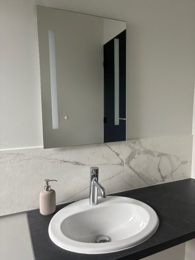 Évier moderne avec robinet, miroir, et distributeur de savon sur un plan de marbre.