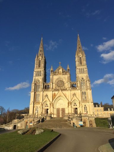 Église avec deux flèches élancées et façade ornée, sous un ciel bleu.
